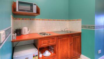 A compact kitchen with a microwave, kettle, sink, and wooden cabinets.