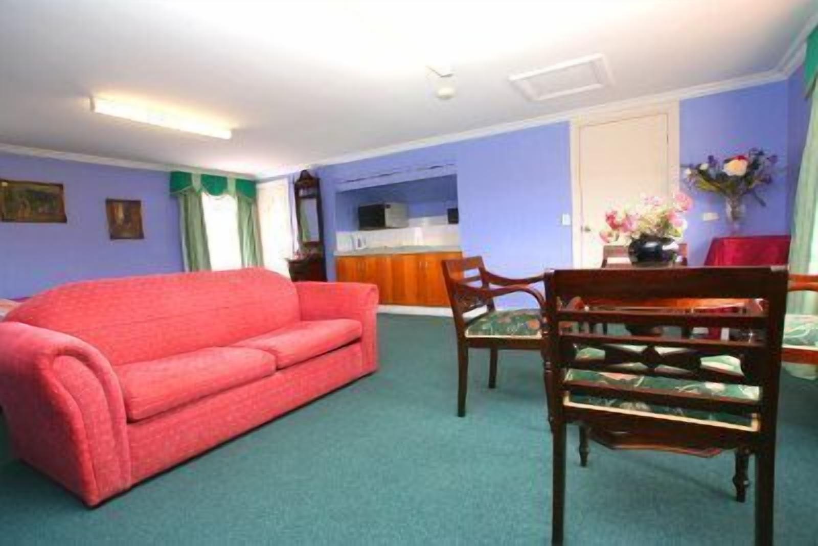 Una habitación con un sofá rojo, una mesa de comedor de madera con sillas, una zona de cocina y una pared azul.