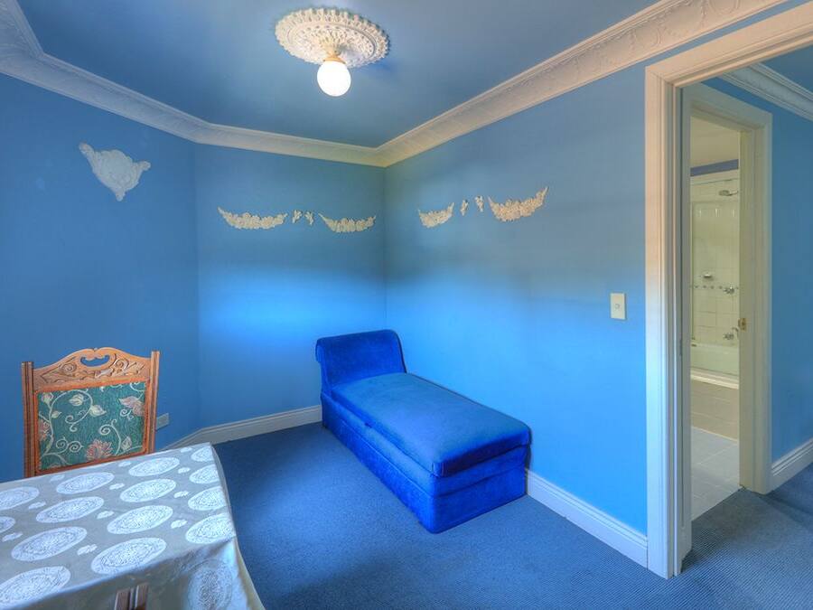 Una habitación con pared azul, un banco pequeño azul, una mesa con estampado y una lámpara decorativa en el techo.