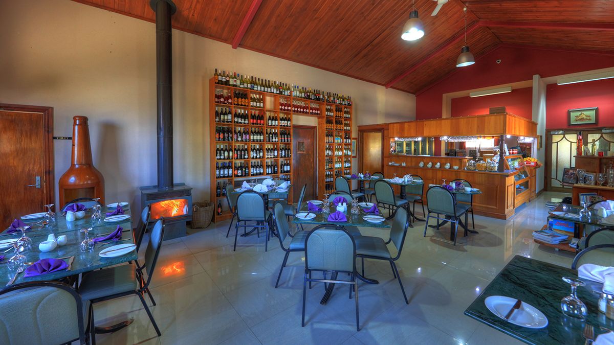 Un restaurante con varias mesas, sillas, una amplia estantería para vinos y una estufa de leña.
