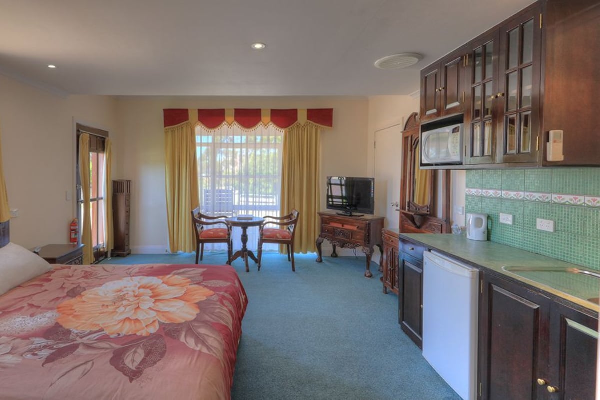 Un dormitorio con una cama grande, un escritorio, televisión y una kitchenette.