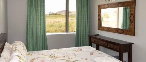 Quarto com cama, mesa de cabeceira, espelho e janela com cortinas.