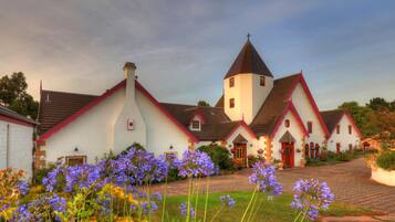 A traditional building with a prominent tower and multiple smaller structures, surrounded by a garden with purple flowers.