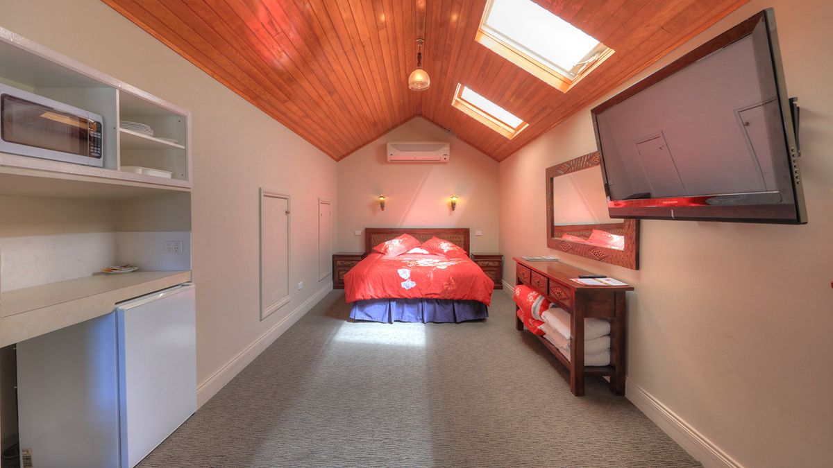 Un dormitorio con cama, televisor montado en la pared, microondas y refrigerador.