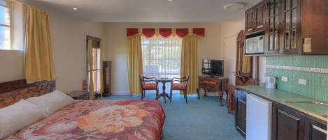 A hotel room with a bed, a dining table, a television, and a kitchenette.
