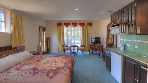 Una habitación de hotel con una cama, una mesa de comedor, un televisor y una kitchenette.
