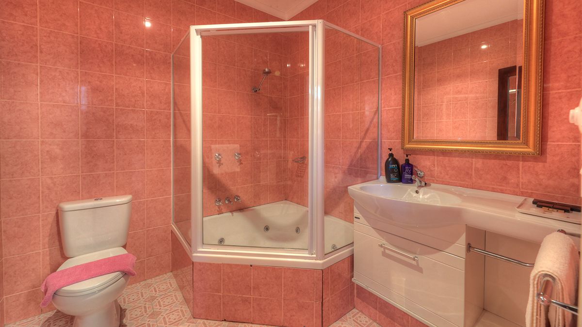 Une salle de bain avec une douche à parois de verre, des toilettes blanches, un lavabo et un miroir avec un cadre doré.