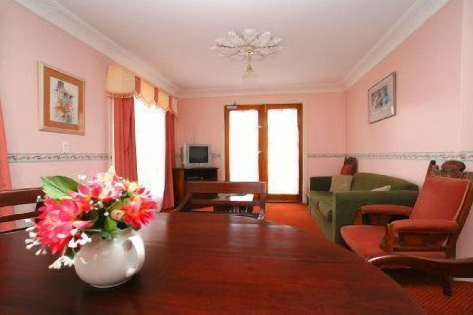 A room with a wooden dining table, a sofa, and a television in the background.