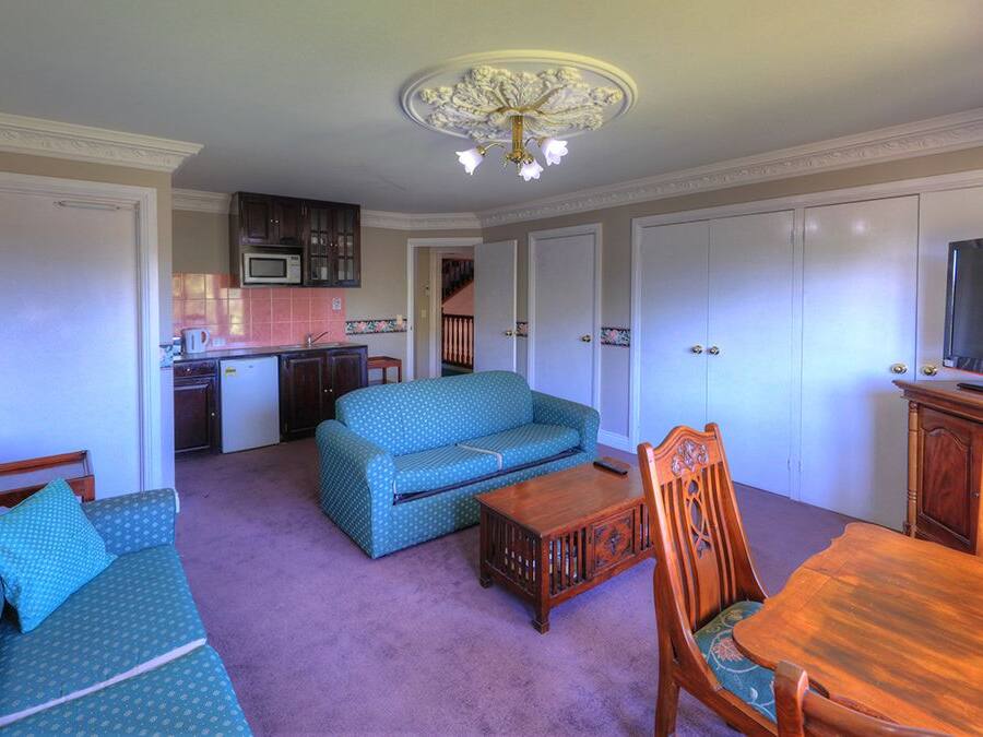 A living room with a sofa, a wooden table, and a TV. There is a kitchen in the background.