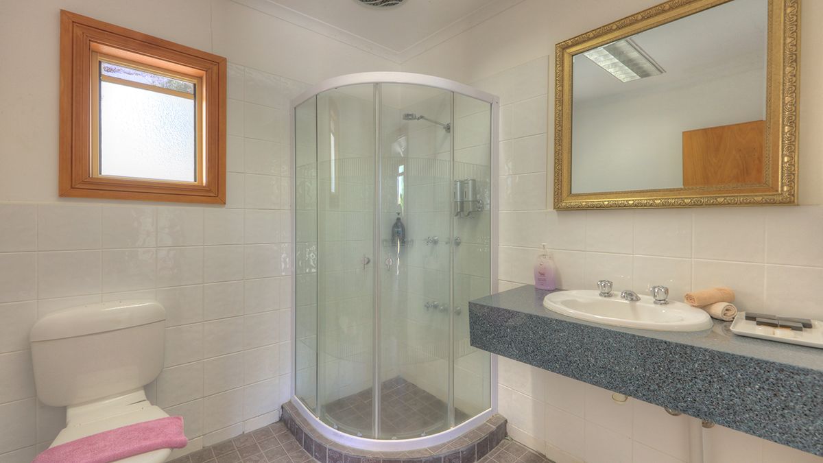 A bathroom with a glass-enclosed shower, a white toilet, a sink with a granite countertop, and a mirror with an ornate frame.
