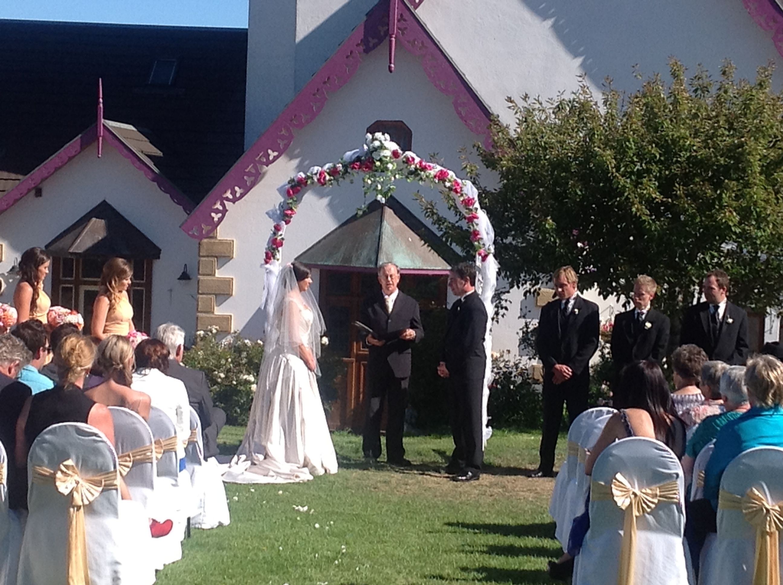 A wedding ceremony outdoors with a white building in the background.