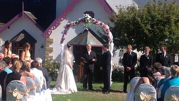 A wedding ceremony outdoors with a white building in the background.