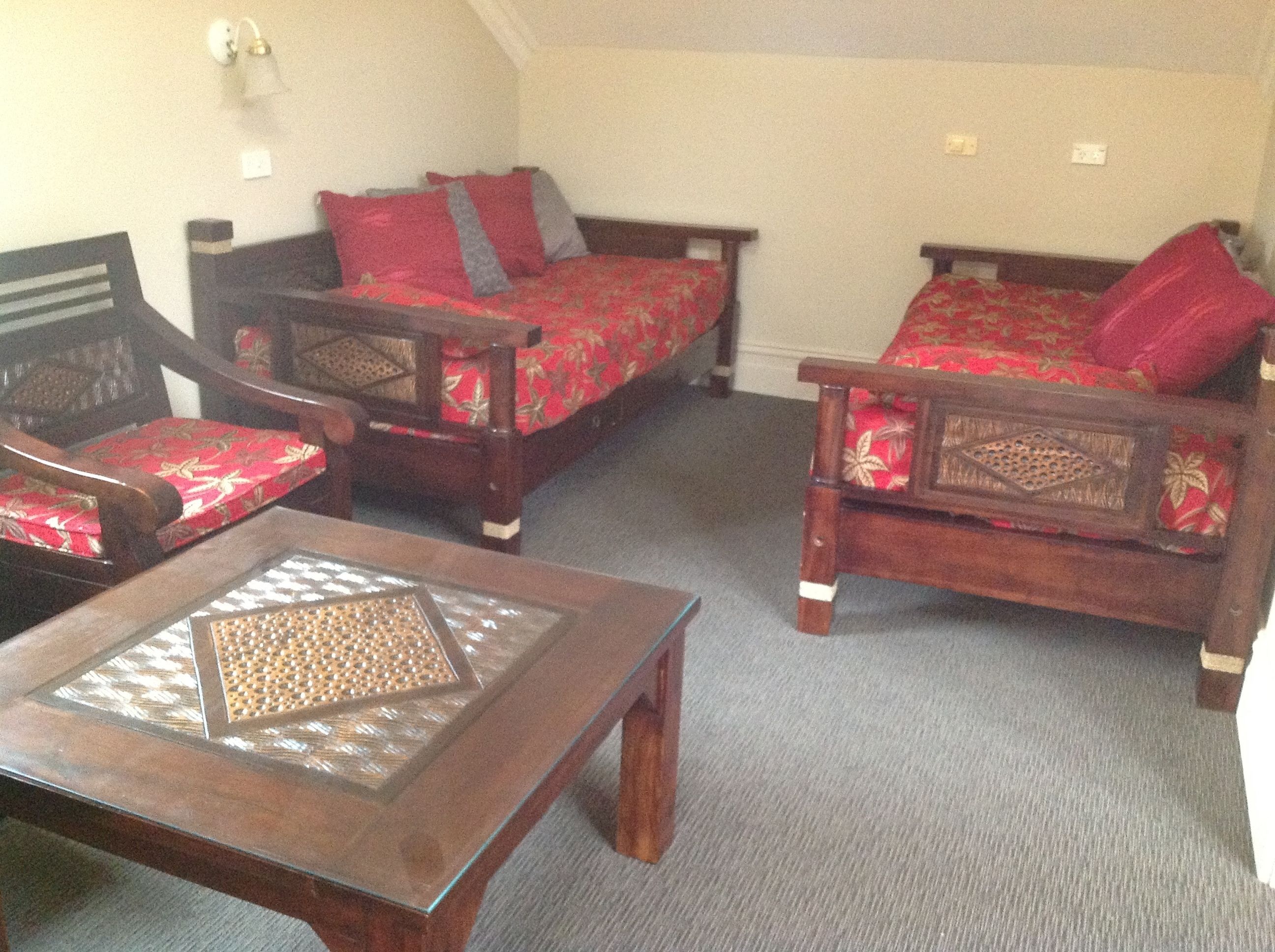 Een kamer met twee houten bedden met rode en grijze beddengoed, een houten stoel met een rood kussen, en een houten tafel met een tafelblad van patroon-glas.