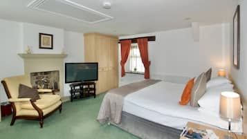 A hotel room with a bed, a television, a fireplace, a chair, and a nightstand with a lamp.