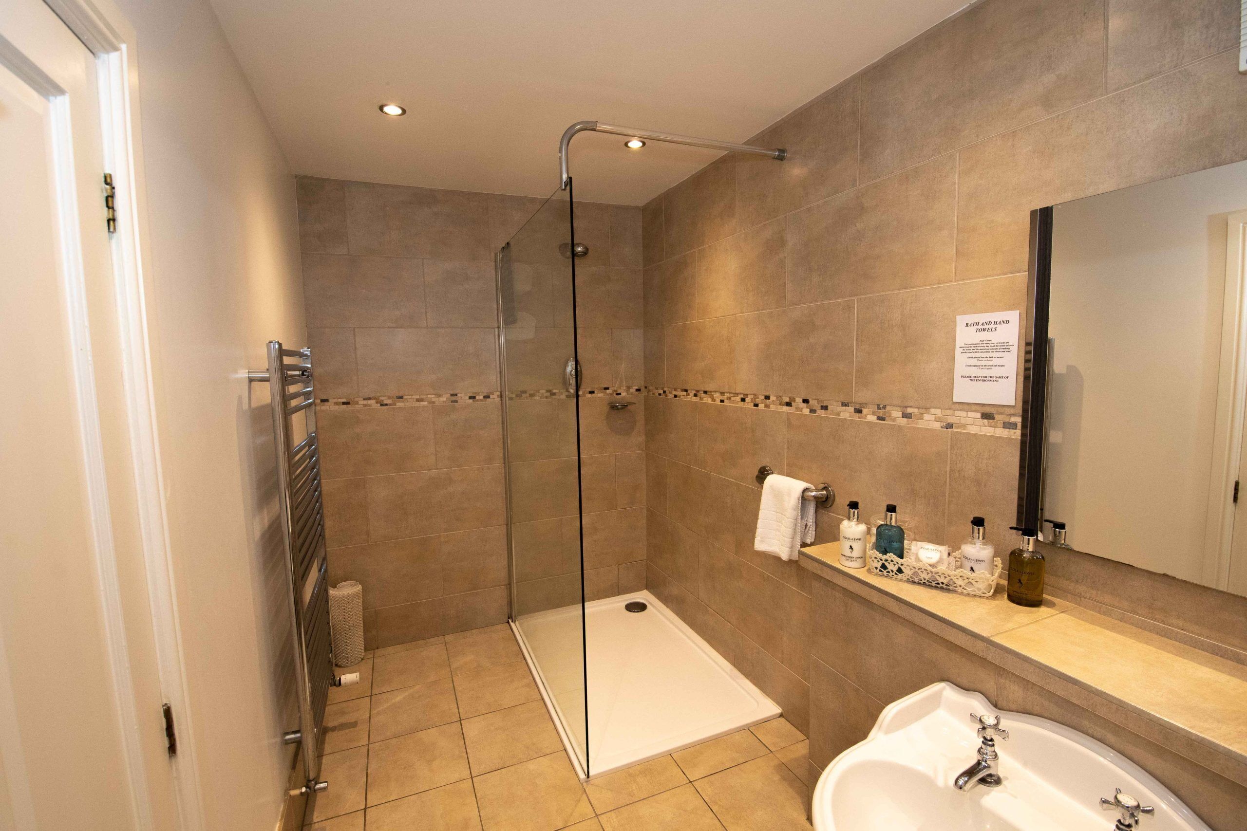 Een moderne badkamer met een douchecabine van glas, een witte wastafel en een meubel met toiletartikelen.