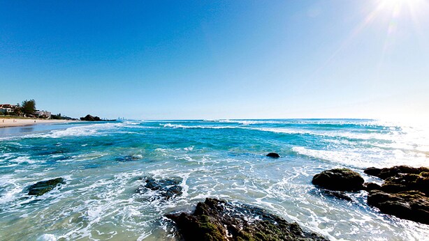 A beach with clear blue water, rocks in the foreground, and a sunny sky. - Sand Castles on Currumbin Beach (Currumbin)