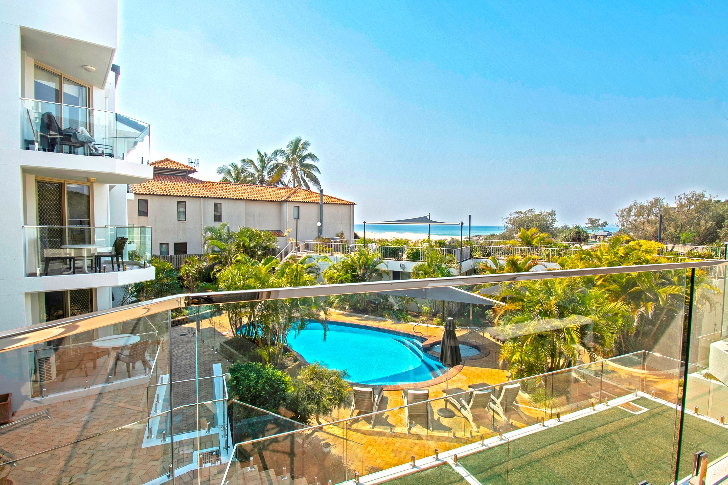 A rooftop pool area with glass railings, a pool, and surrounding greenery.