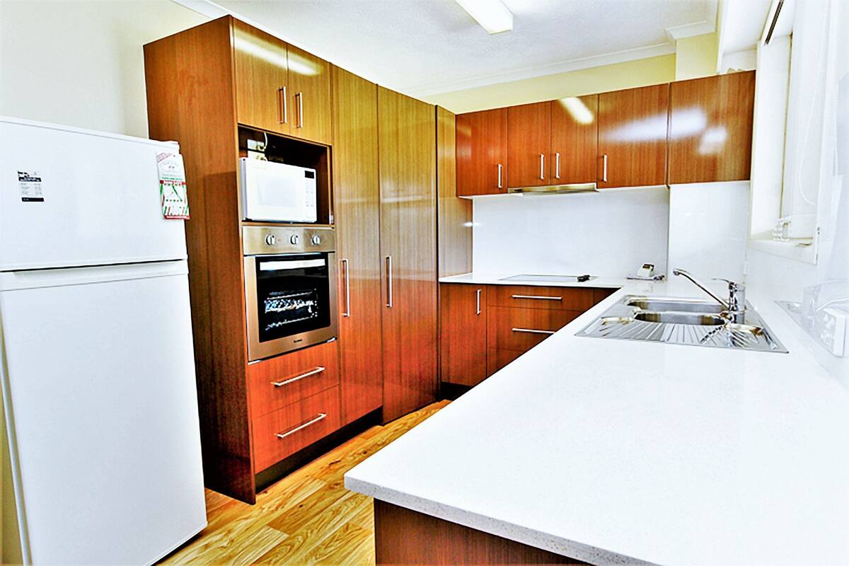 A modern kitchen with wooden cabinets, a white refrigerator, an oven, and a sink.
