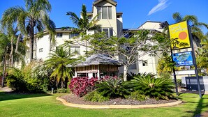 A two-story building with a large balcony, surrounded by tropical vegetation and palm trees. - Sand Castles on Currumbin Beach (Currumbin)