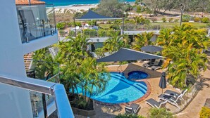 A rooftop pool with lounge chairs and umbrellas, surrounded by palm trees and a view of the beach. - Sand Castles on Currumbin Beach (Currumbin)