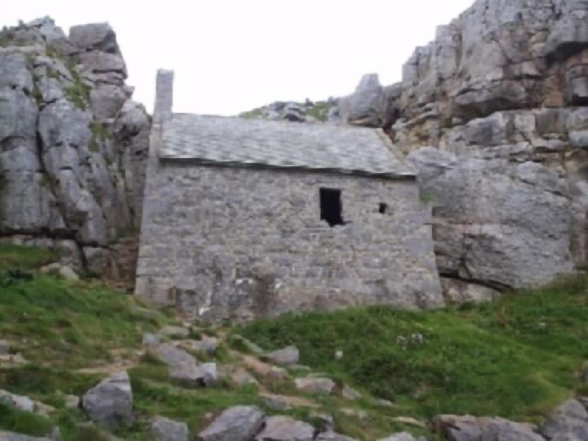 Un pequeño edificio de piedra con una sola ventana, rodeado de terreno rocoso.