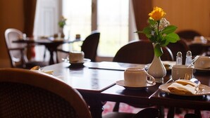 Ein Esstisch ist gedeckt mit einer weißen Tasse, einem Untertasse und einem gefalteten Servietten. Auf dem Tisch steht eine Vase mit einer gelben Blume.