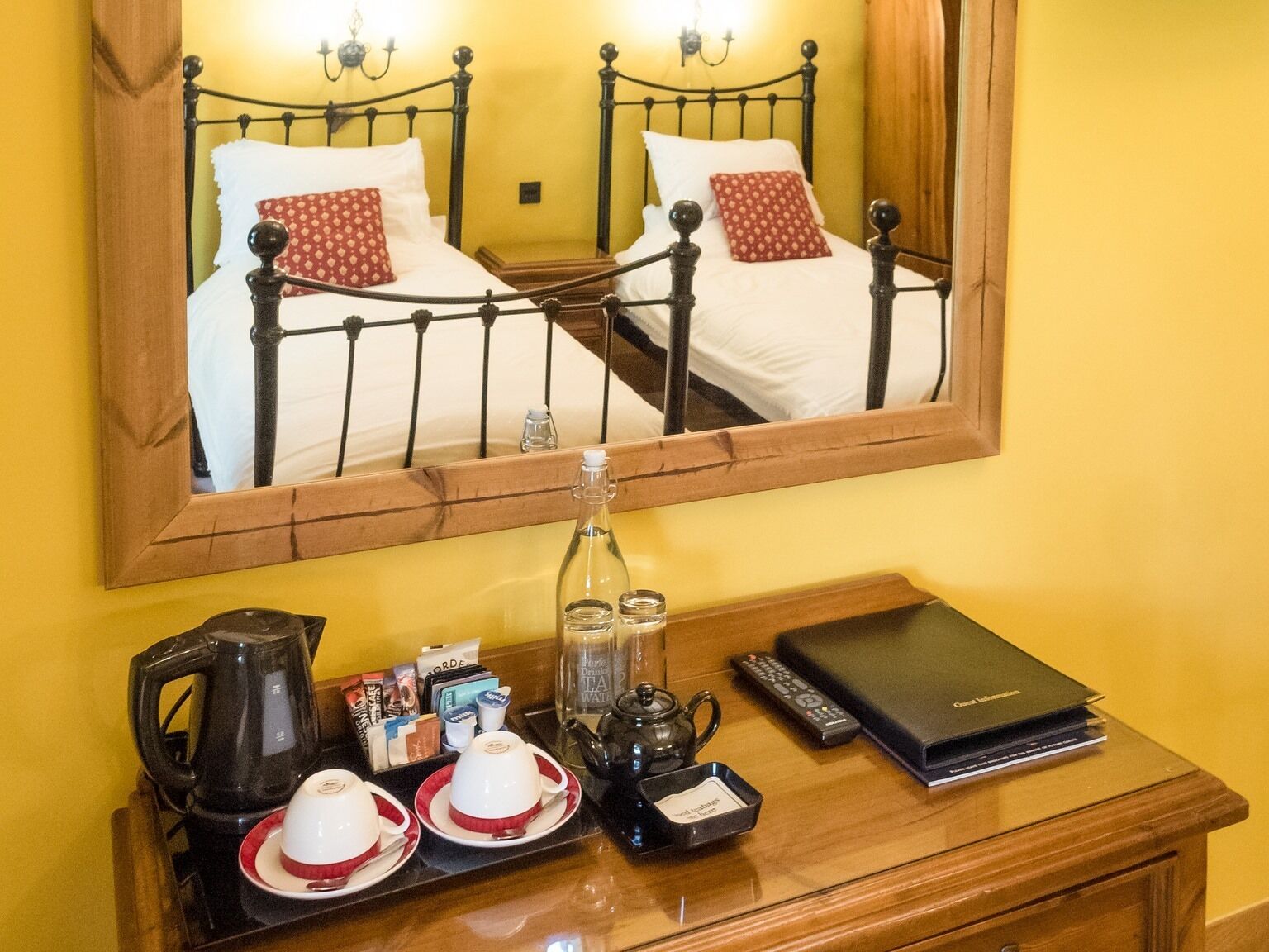 Una habitación de hotel con una cama, una mesita de noche con tetera, tazas y un control remoto.