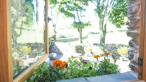 A view through a window with a stone wall and a garden with various flowers. - The Wayside and Whisky Barn (Millom)
