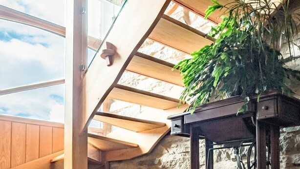 A room with a sloped ceiling, wooden beams, a stone wall, and a table with a potted plant. - The Wayside and Whisky Barn (Millom)