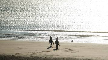 Una spiaggia con una persona a cavallo e un'altra che cammina accanto.