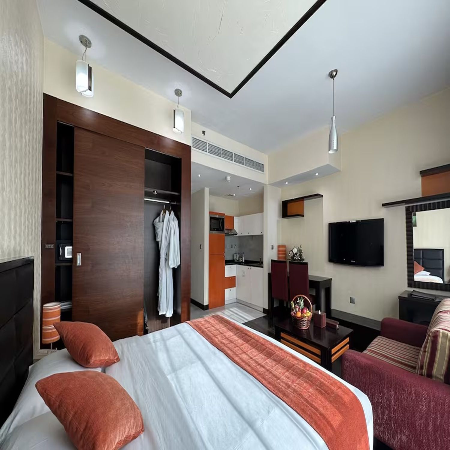 A hotel room with a bed, a wardrobe, a kitchenette, a TV, and a seating area.