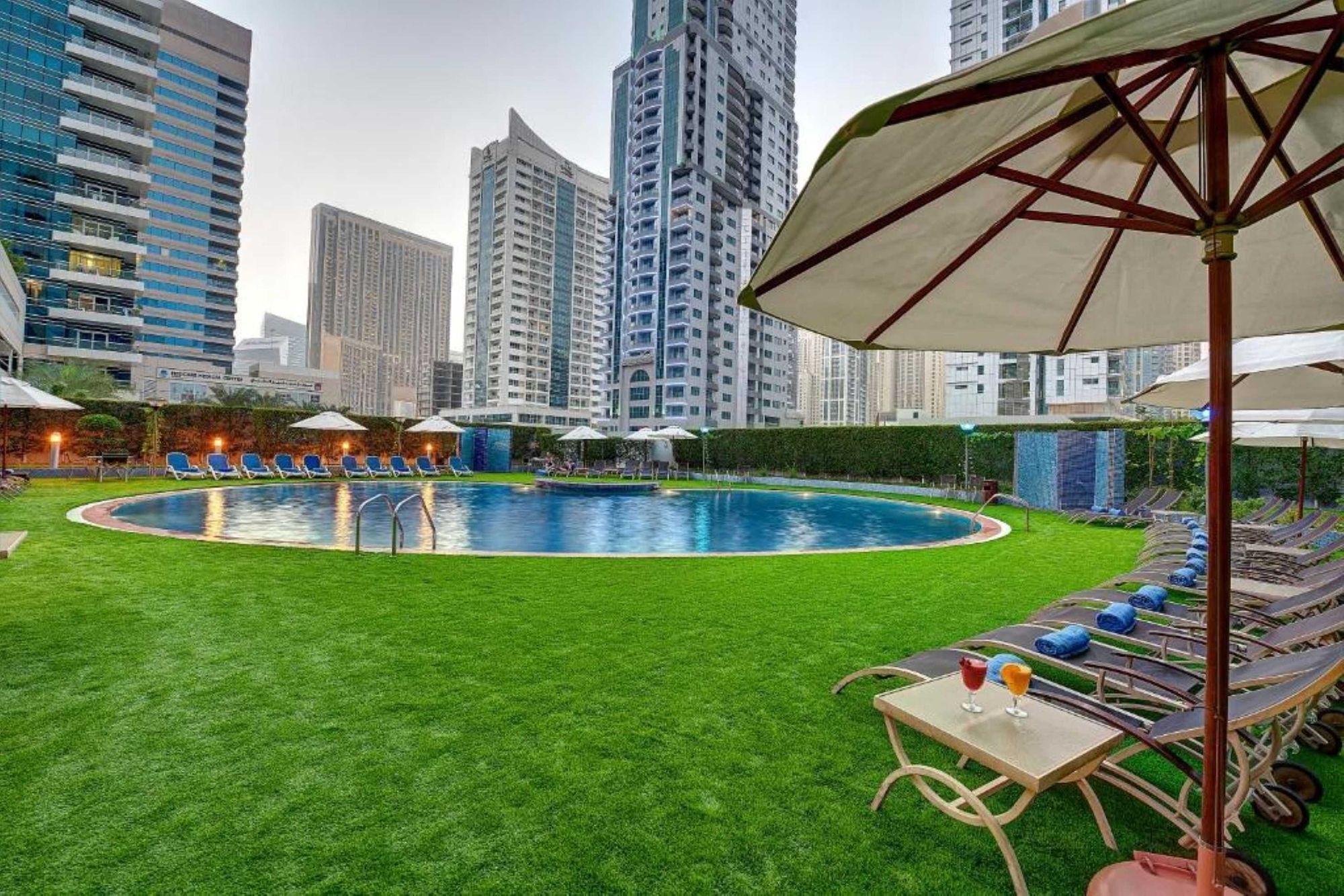 Una piscina con un área verde circundante, sillas de descanso y sombrillas.