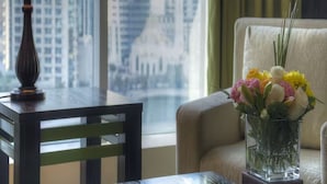 A room with a table, a lamp, a vase with flowers, a chair, and a view of a cityscape through large windows. - Sunday Marina View Hotel Apartments (Dubai)