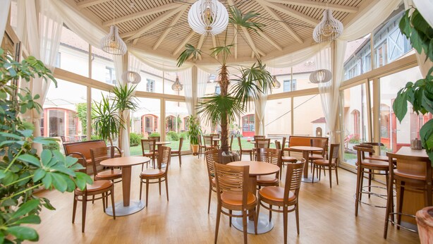 A spacious indoor area with wooden tables and chairs, large windows, and hanging light fixtures. - JUFA Hotel Pöllau (Poellau)