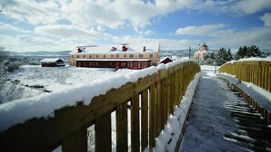 A snow-covered wooden bridge leading to a building with a red facade and a dome structure in the background. - JUFA Hotel Pöllau (Poellau)