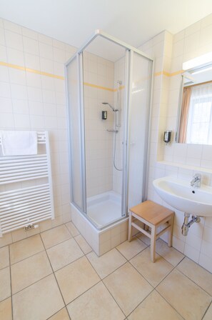 A bathroom with a glass-enclosed shower, a wooden stool, a white sink, and a towel rack. - JUFA Hotel Pöllau - Self Check-in (Poellau)