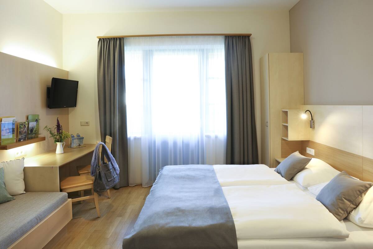 A hotel room with a bed, a desk, a chair, a television, and a window with curtains.