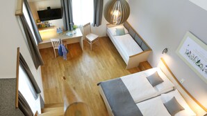A modern hotel room with a wooden floor, a desk with a chair, a bed with two pillows, a bedside table, and a wall-mounted TV. - JUFA Hotel Pöllau (Poellau)