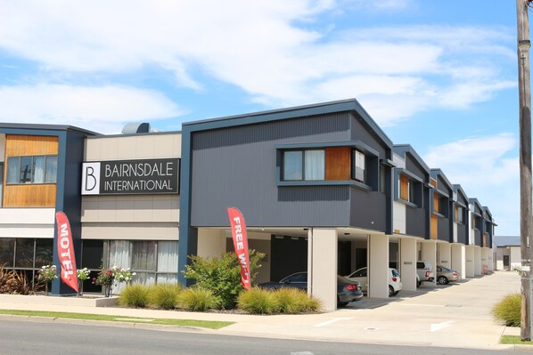 A modern motel with a sign reading "Bairnsdale International" and "Free WiFi" flags.