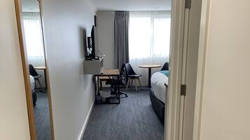 A hotel room with a large mirror, a desk with a chair, a bed, and a small table.