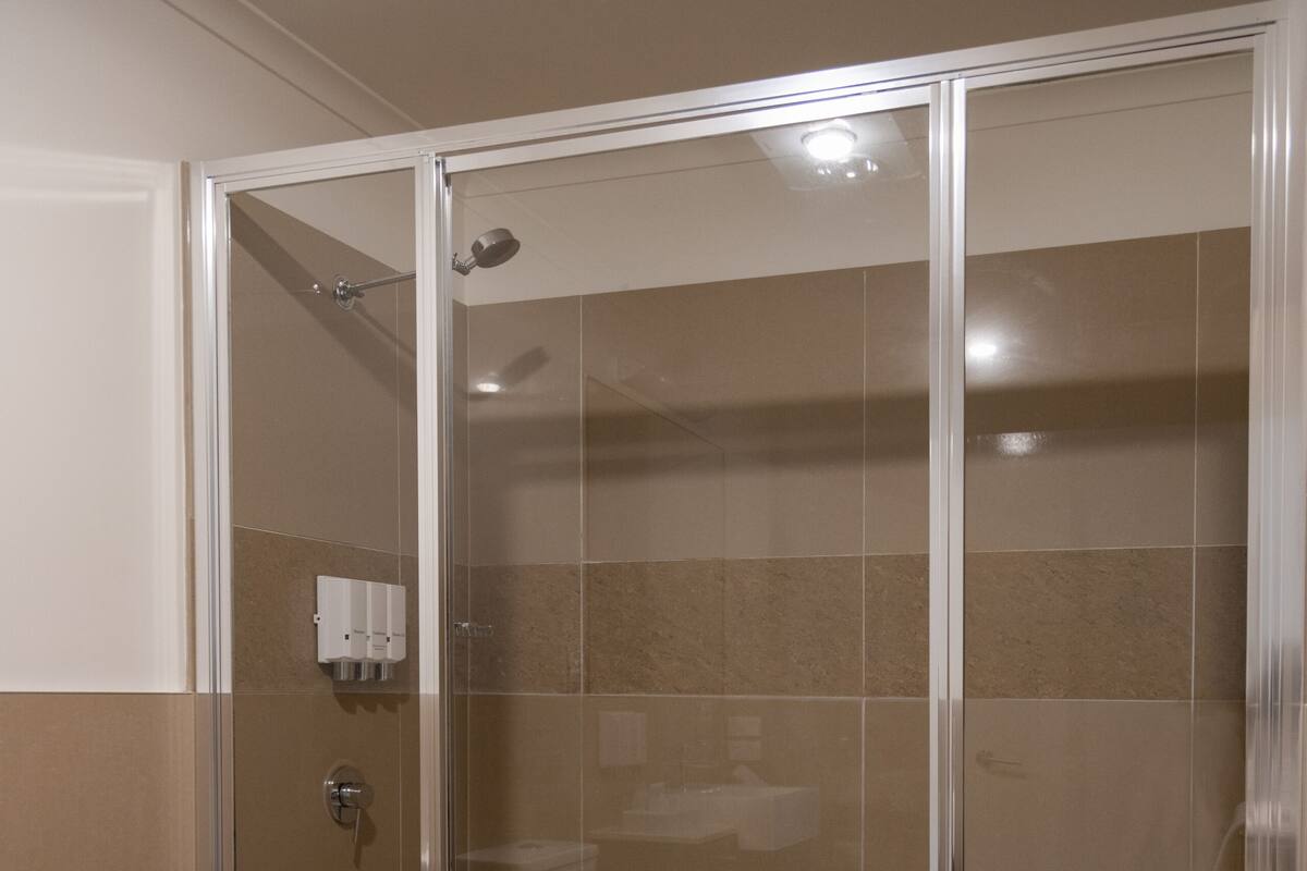 Une douche fermée par des parois de verre, avec une baignoire blanche, des carreaux de couleur beige et une serviette blanche posée sur le sol.