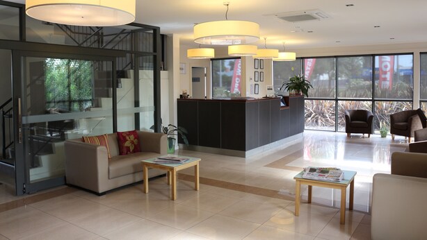 A modern hotel lobby with a reception desk, seating area, and large windows offering a view of the outdoors.