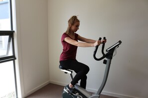 Eine Person fährt ein Ergometer in einem Raum mit großem Fenster und schlichten Wänden.