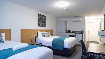 Habitación de hotel con dos camas, un escritorio, una silla, una kitchenette y un baño.