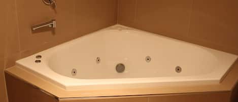 A rectangular hot tub with a control panel on the left, set against beige tiled walls.