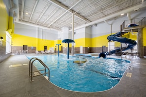 An indoor swimming pool with a blue slide, seating areas, and a high ceiling with visible structural beams.