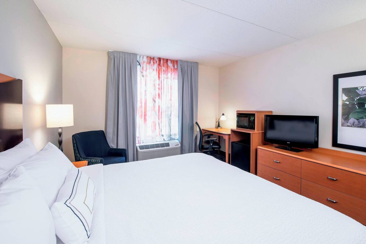 A hotel room with a bed, a desk with a computer, a television, and a window with curtains.