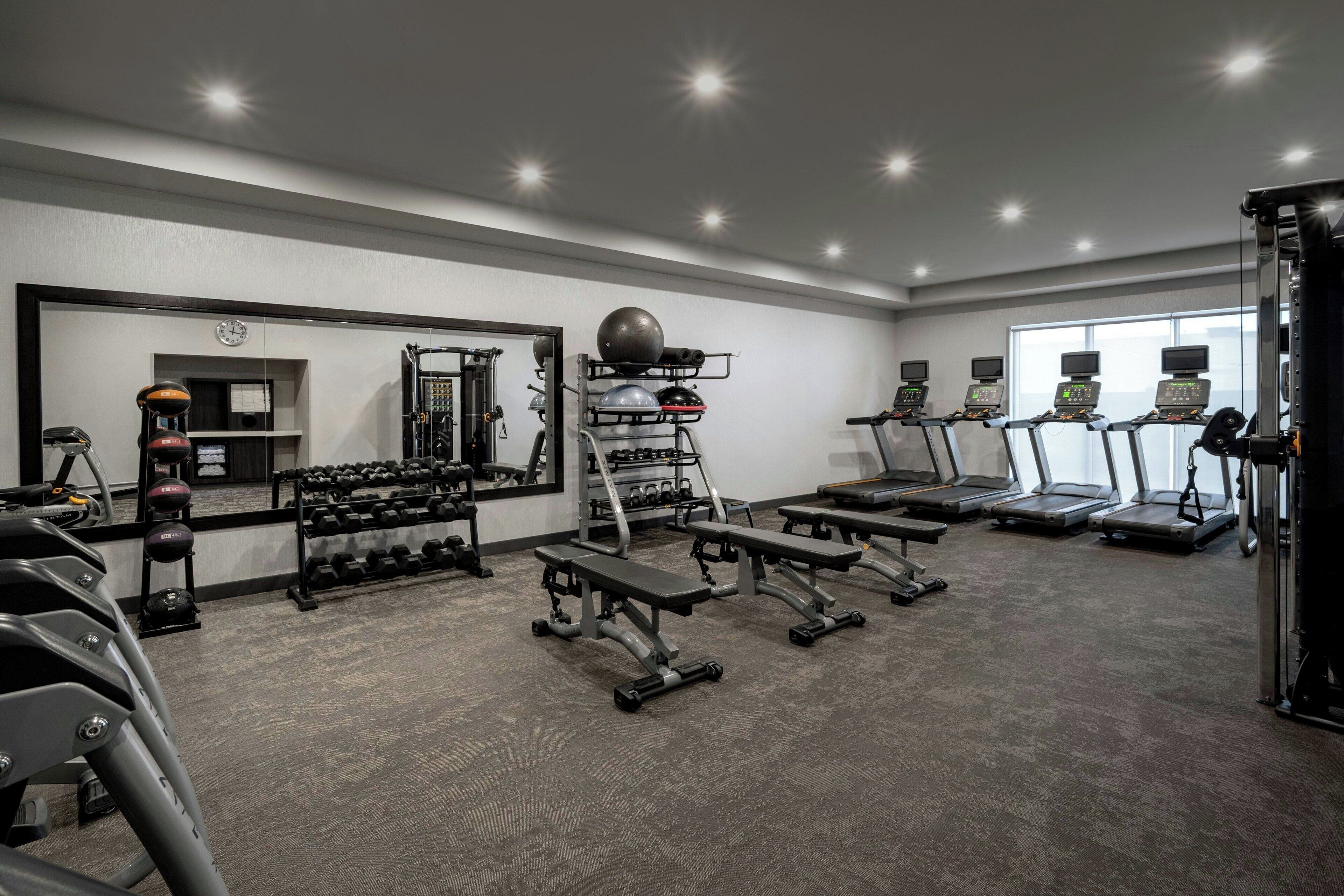 A gym with treadmills, weight benches, dumbbells, and a mirrored wall.