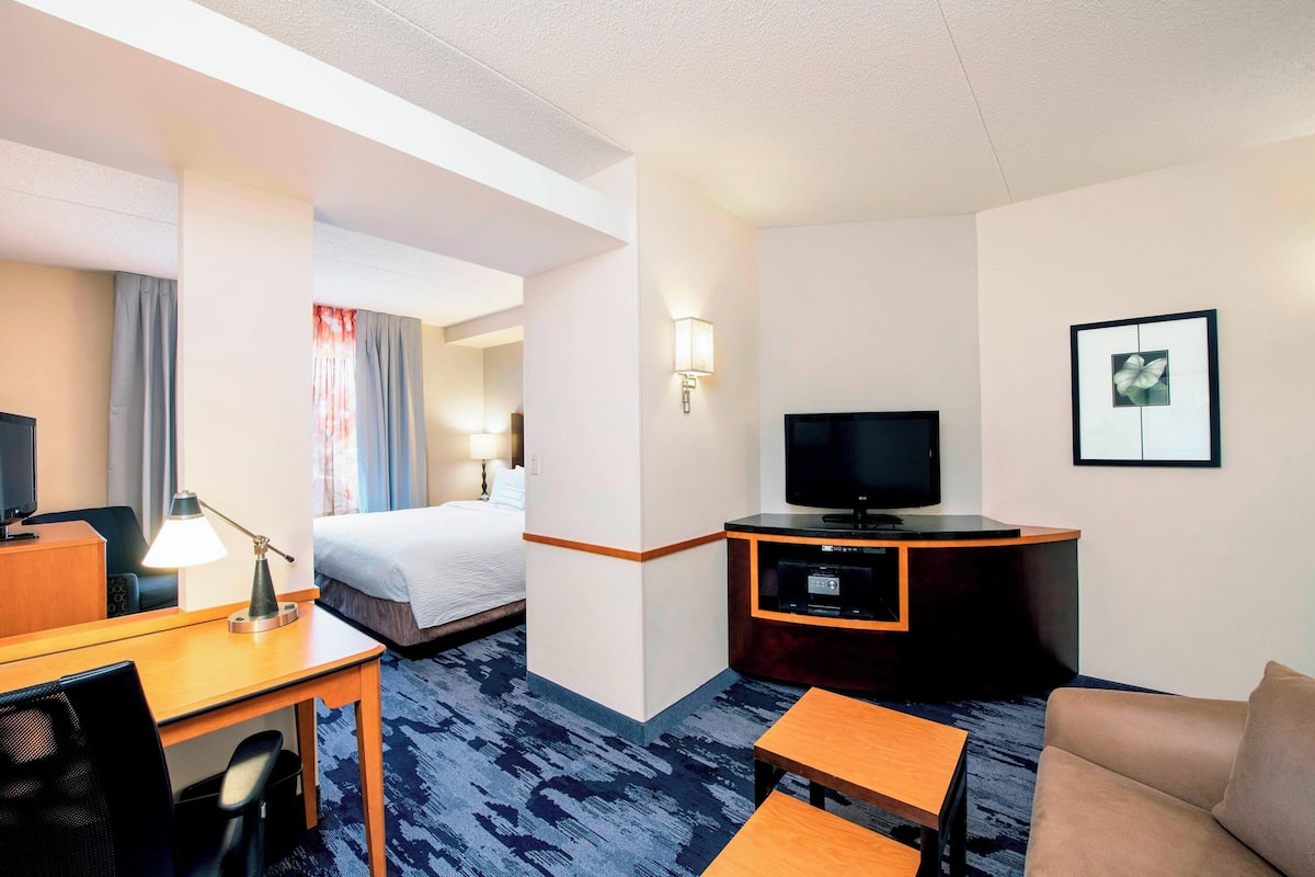 A hotel room with a bed, desk, chair, TV, and a small table.