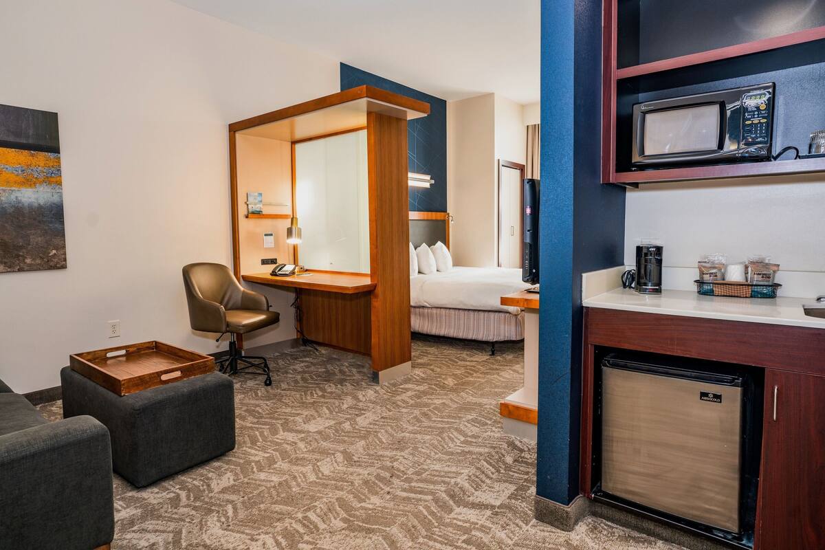 Une chambre d’hôtel comprenant un lit, un bureau, une chaise, une petite kitchenette et un four à micro-ondes.